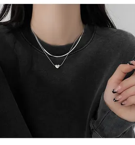Detailed view of a silver double-layered necklace featuring heart pendant and snake chain