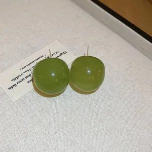Close-up view of forest green round resin stud earrings with silver needles.