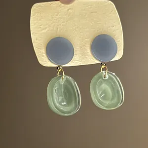 Close-up of forest style resin earrings with green translucent dangles and blue studs.