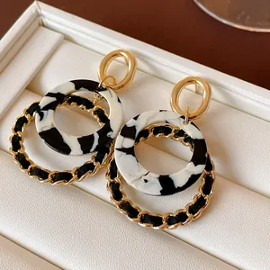 Close-up of geometric round dangle earrings with gold chain and black marble resin