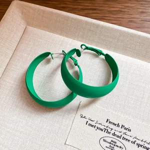 Close-up of matte forest green hoop earrings with silver pins on a beige textured jewelry tray