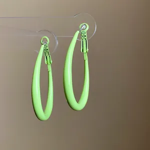 Macro view of lime green teardrop hoop earrings on a minimalist transparent stand.