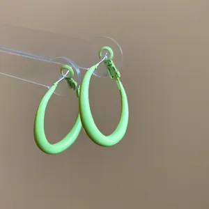 Close-up of lime green spray-painted oval hoop earrings on a clear acrylic display stand