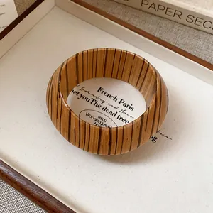 Close-up of a vintage-style bangle featuring a vertical wood grain pattern in a wooden tray.