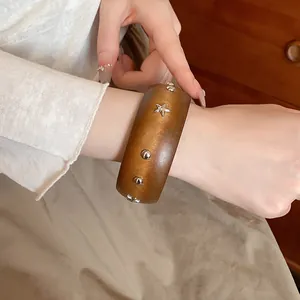 Close-up of vintage wooden bangle with silver star and stud embellishments on wrist