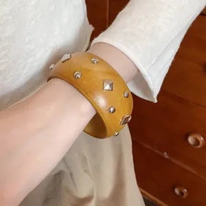Macro detail of a wide wooden bangle adorned with square and round silver studs