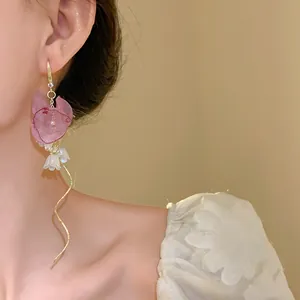 Close-up of pink chiffon flower and pearl tassel drop hook earrings worn by a model