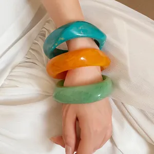 Close-up detail of three marbled resin spiral bangles in teal, orange, and mint green