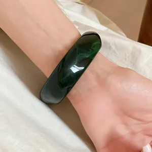 Detailed close-up of a dark green swirled resin square bangle worn on a female wrist