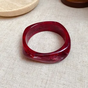 Close-up detail of a dark red marbled resin bangle featuring a unique square spiral shape