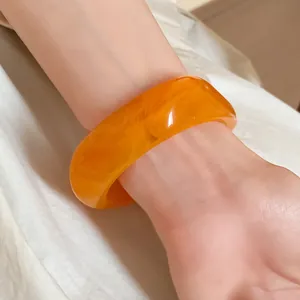 Close-up of a chunky orange resin bangle with marbled swirl pattern on wrist