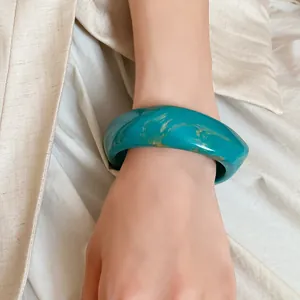 Close-up view of a stylish turquoise marbled resin spiral bangle worn on a woman's wrist