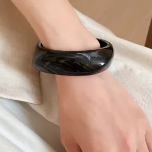Detailed shot of a stylish black marbled resin square spiral bangle worn on a wrist