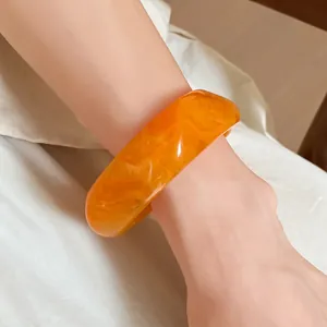 Close-up of a stylish orange marbled resin square bangle worn on a model's wrist.