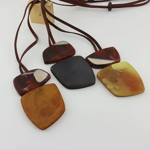 Macro detail of oversized geometric marbled resin pendants on brown faux-leather cords.