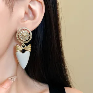 Detail view of vintage style gold earrings with white heart drop and rhinestone bow