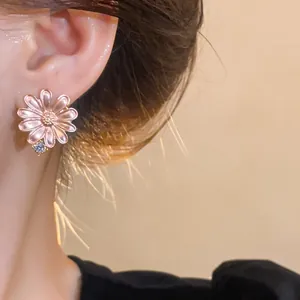 Close-up of elegant pink daisy stud earrings with zircon stones worn by a model in soft light