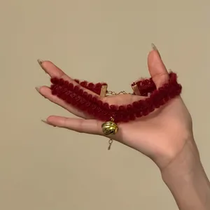 Détail d'un choker festif en dentelle bordeaux avec un pendentif clochette dorée.