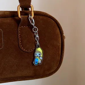 Close-up shot of a cute banana cat acrylic keychain charm hanging on a brown suede bag