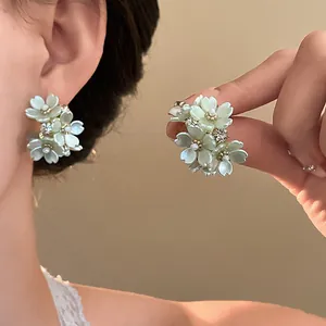 Close-up of floral rhinestone stud earrings in light green being held and worn.