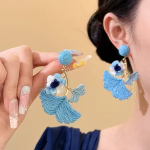 Detail view of blue raffia flower and ginkgo leaf earrings with elegant design.