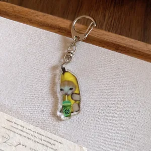 Close-up of a cute acrylic Banana Cat keychain with a green drink cup on white background.