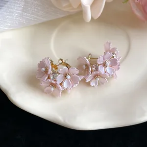 Close-up of pink cherry blossom earrings with sparkling crystals and pearls on a white plate
