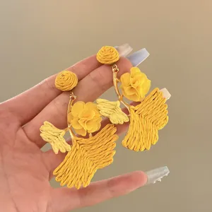 Detailed view of yellow raffia ginkgo leaf earrings with fabric flower accents.