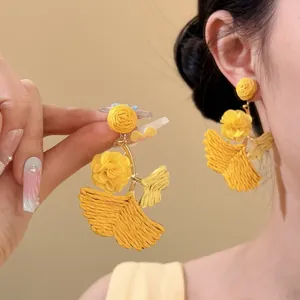 Close-up detail of yellow raffia flower earrings with ginkgo leaf charm worn on ear