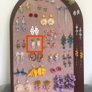 Green bead and shell disc drop earrings displayed on a jewelry board among various floral designs