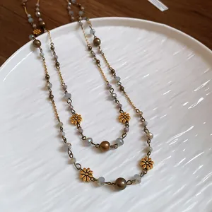 Boho-Halskette im Ethno-Stil mit goldenen Blumenanhängern auf weißem Keramikteller