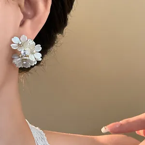 Close-up of elegant flower stud earrings with white petals and rhinestones on ear