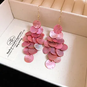 Detailed view of pink shell tiered tassel earrings with round discs and gold hooks