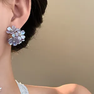 Elegant purple flower stud earrings with crystal center shown on an Asian model's ear