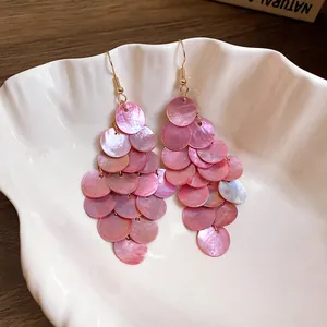 Detailed view of pink shell round tassel earrings resting in a white shell-shaped dish