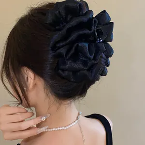 Detail of a large black ruffled fabric hair claw clip styled on a low bun