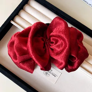 Close-up view of a shimmering deep red pleated fabric bow hair claw clip in a display box