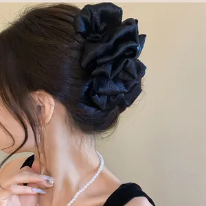 Detailed view of an elegant black fabric pleated flower hair claw clip worn on a model hair bun