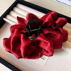 Detail view of a large pleated dark red fabric hair claw clip placed in a jewelry box