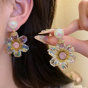Close-up of elegant flower pendant earrings with iridescent resin petals and pink crystal.