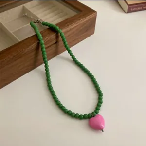 Close-up of green beaded necklace with a pink heart-shaped pendant on a desk