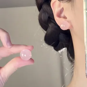 Close-up detail of a pink translucent bead stud earring worn on ear with dark hair