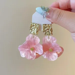 Close-up of pink resin flower earrings with textured gold studs and silver pins.
