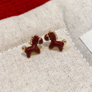 Elegant red enamel horse stud earrings with 18K gold plating on linen background