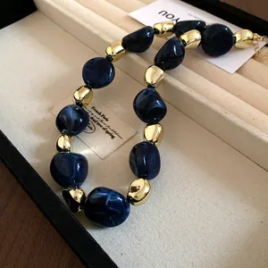 Macro detail of irregular blue marbled beads and gold metallic necklace in a box