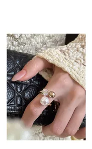Primo piano di un anello aperto dorato con zircone e perle irregolari indossato su una mano.