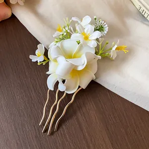 Pique à cheveux élégante avec fleurs de frangipanier en tissu blanc et peigne doré ondulé.