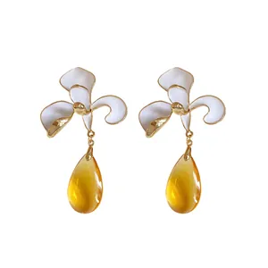 Elegant flower teardrop earrings with white enamel petals and amber drops on white background.