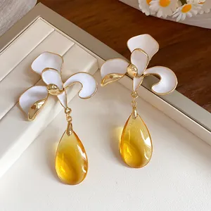 Macro view of white enamel flower drop earrings with amber translucent teardrop pendants