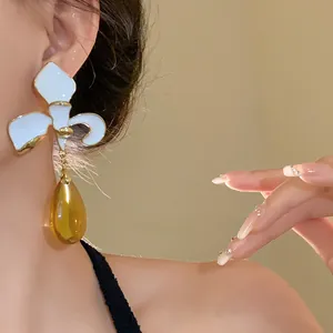 Detailed view of elegant white enamel flower earring with an amber resin teardrop pendant
